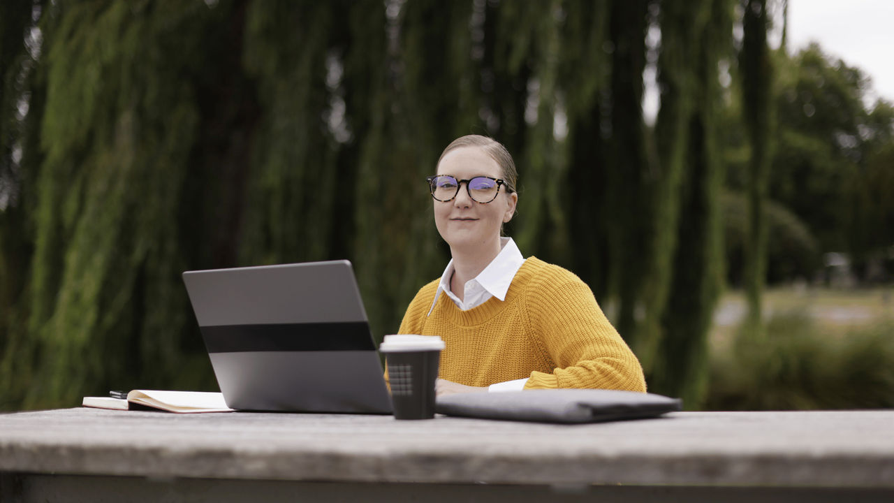 A young woman in a yellow sweater sits at a picnic table, using a laptop to complete an online study session.