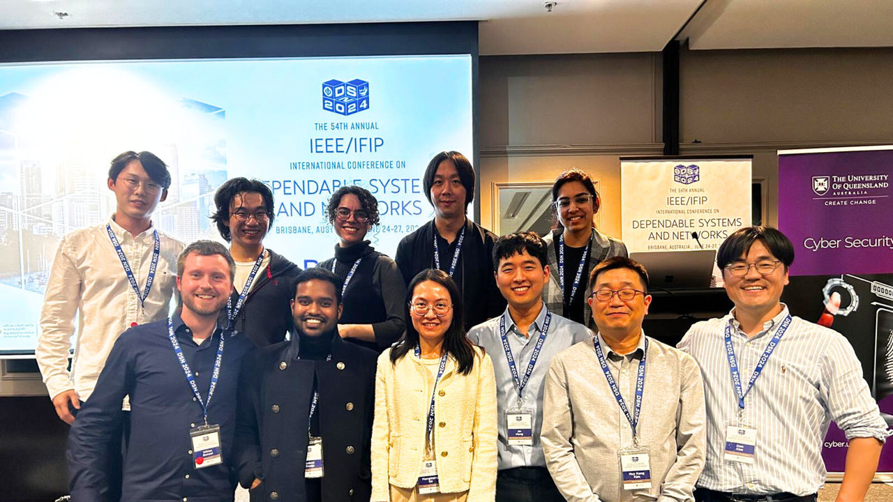 Group of people in front of a large screen at a conference including Dr Ke He | UC Online