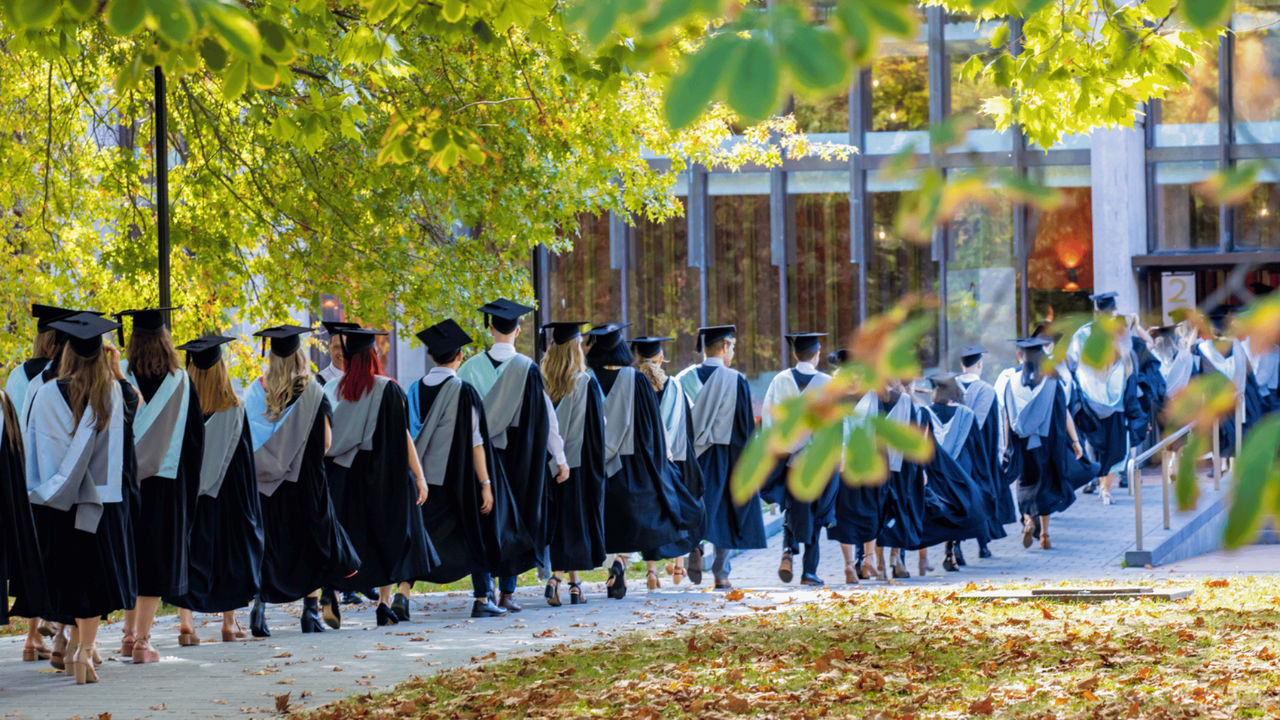 A row of University of Canterbury graduates, wearing academic regalia, file into the Christchurch Town Hall.