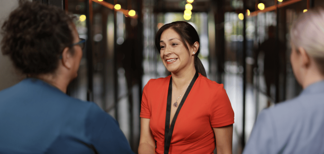 A professional woman greets UC Online team members before a meeting about staff training and development options.