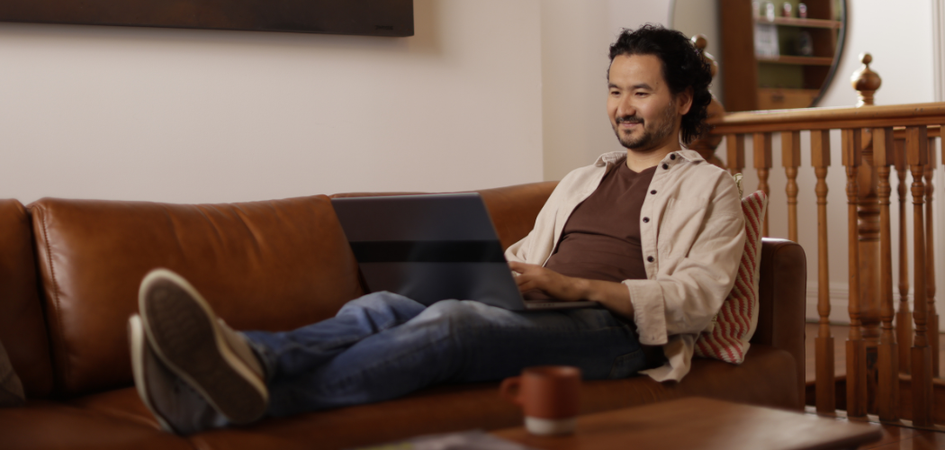 A UC Online student sits in a relaxed position on the couch, laptop on his lap, enjoying the flexibility of online learning.