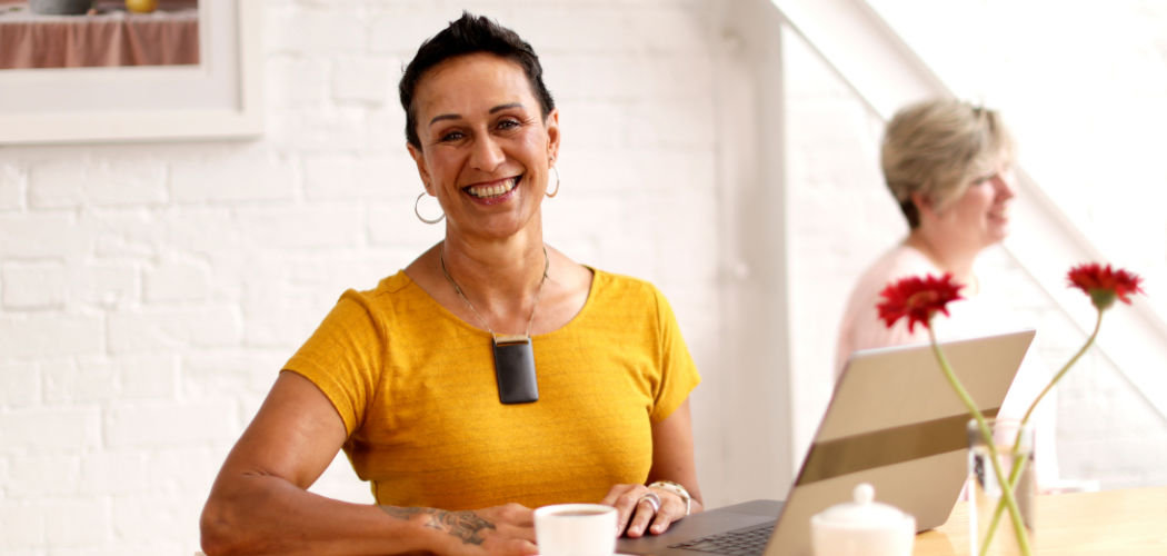 Woman in a yellow t-shirt smiling as she studies project management online with the University of Canterbury UC Online