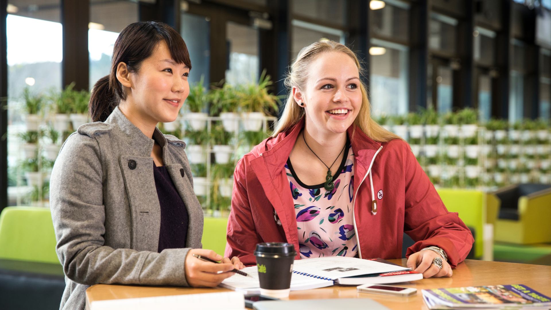 Two female teachers studying AI Essentials for Educators course online together in a cafe environment