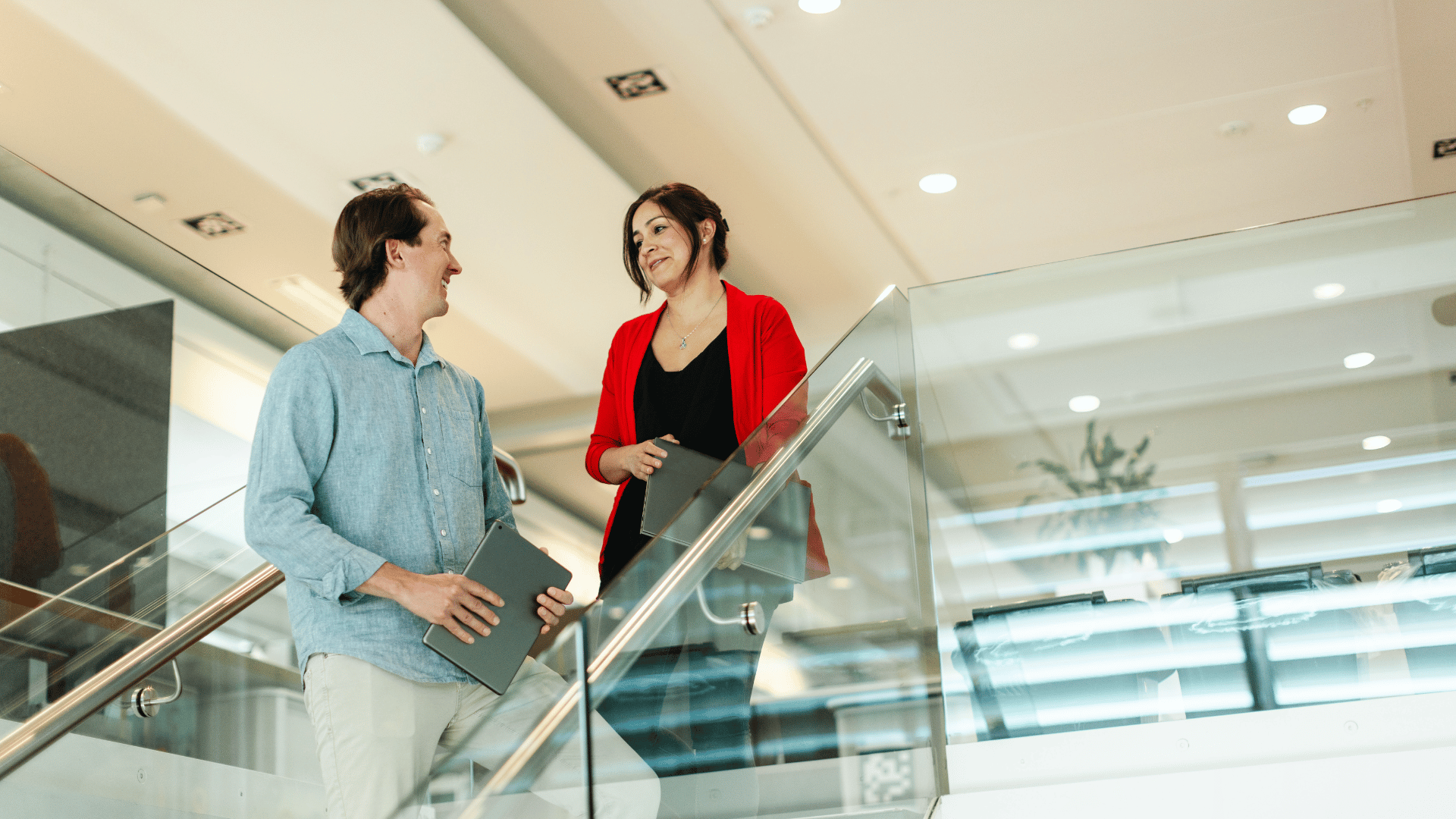 Two professionals walk downstairs, stopping to discuss AI gains they've made after studying AI online. 