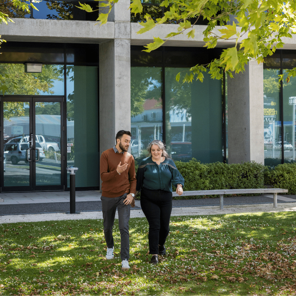 A young man and woman walking outside in a green space, discussing wellbeing