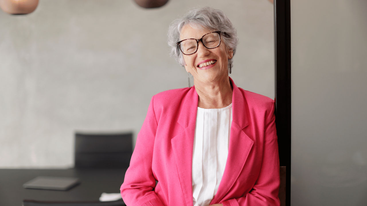 Woman with grey hair in a pink blazer smiling after successfully leading her business and management meeting.