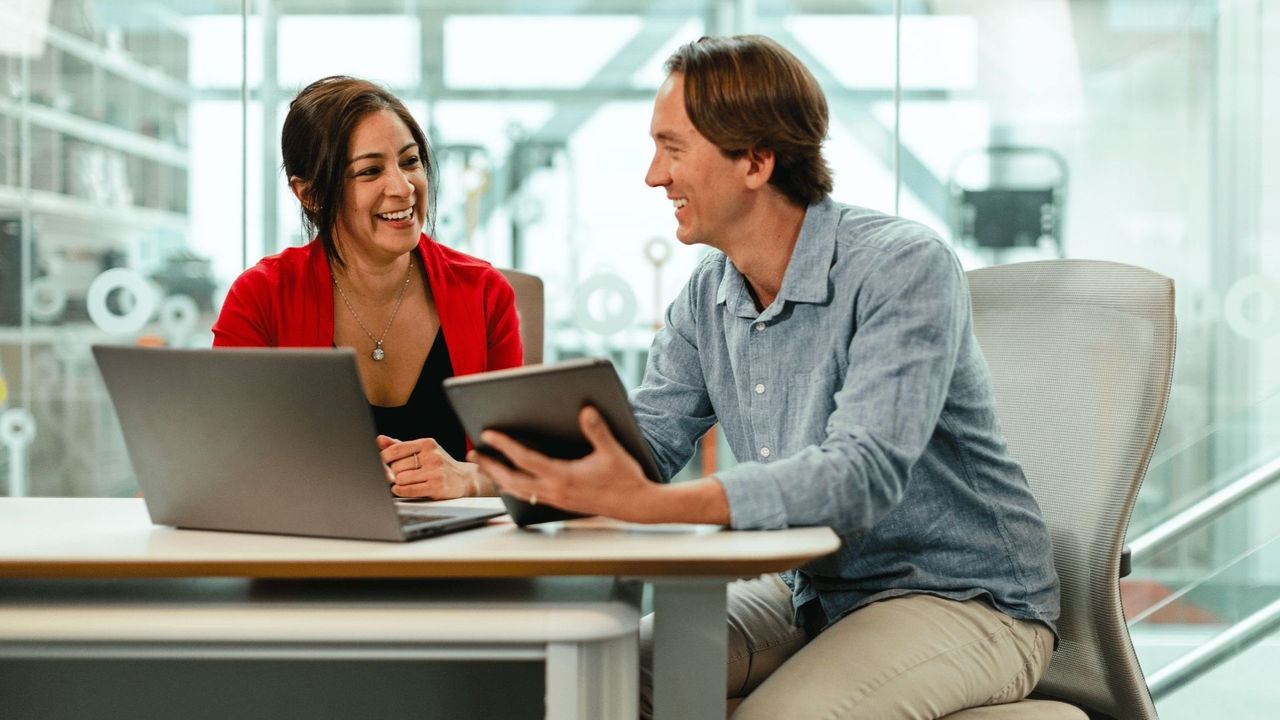 Two colleagues smiling at a desk, comparing AI training results from their generative AI prompt. 