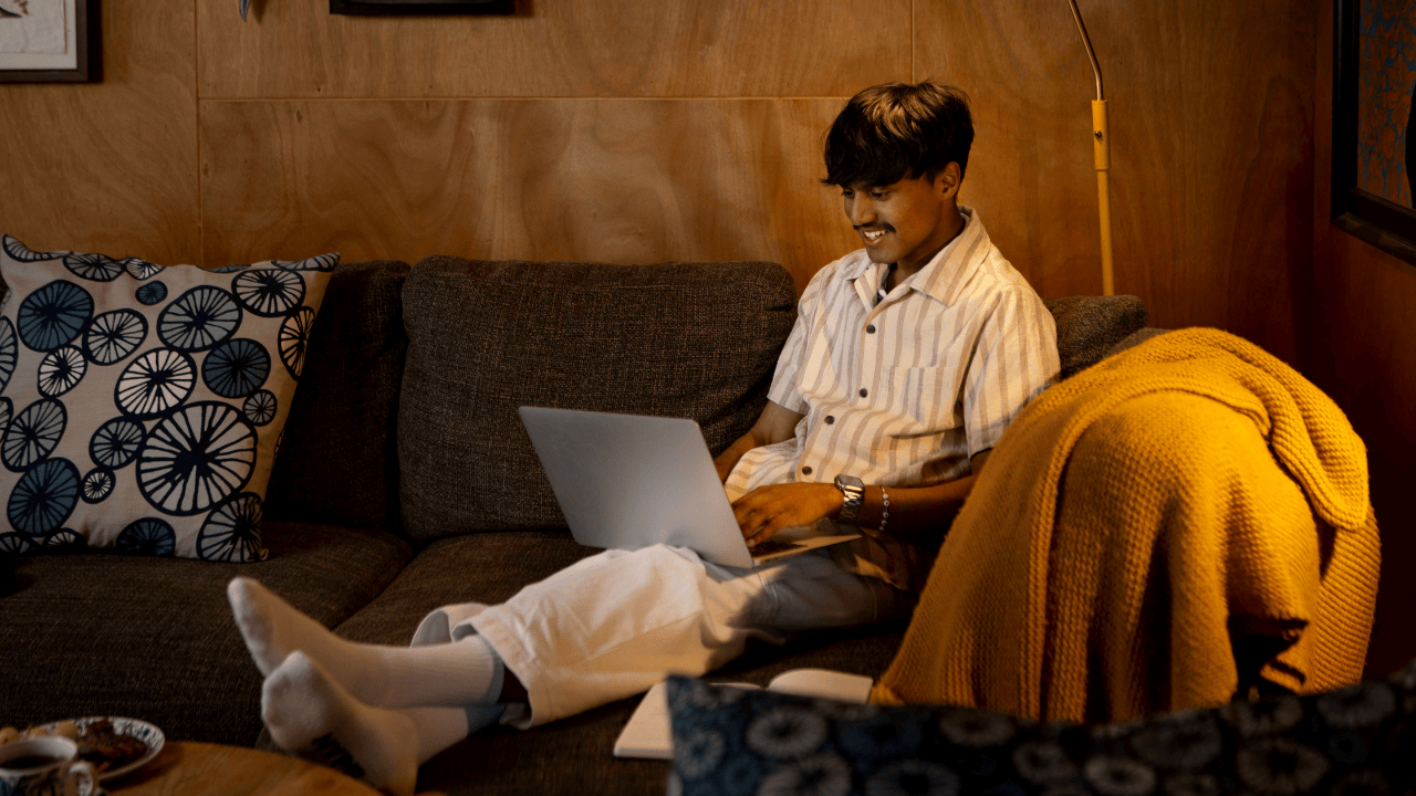 A UC Online student sits in a relaxed position on the couch, laptop on his lap, enjoying the flexibility of online learning.