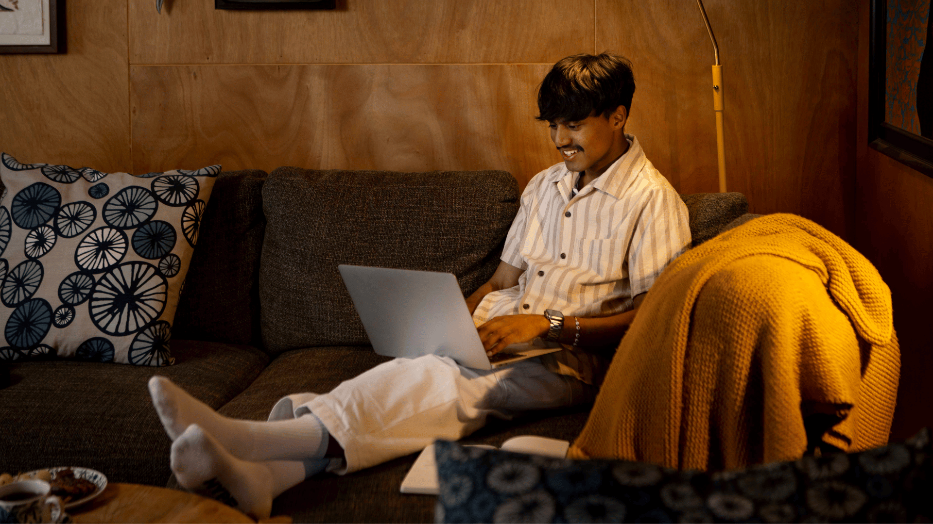 A UC Online student sits in a relaxed position on the couch, laptop on his lap, enjoying the flexibility of online learning.