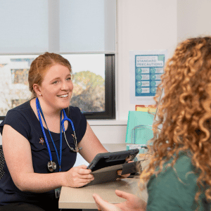 A Master of Advanced Nursing (Nurse Practitioner) student works at a computer in a clinical healthcare setting.