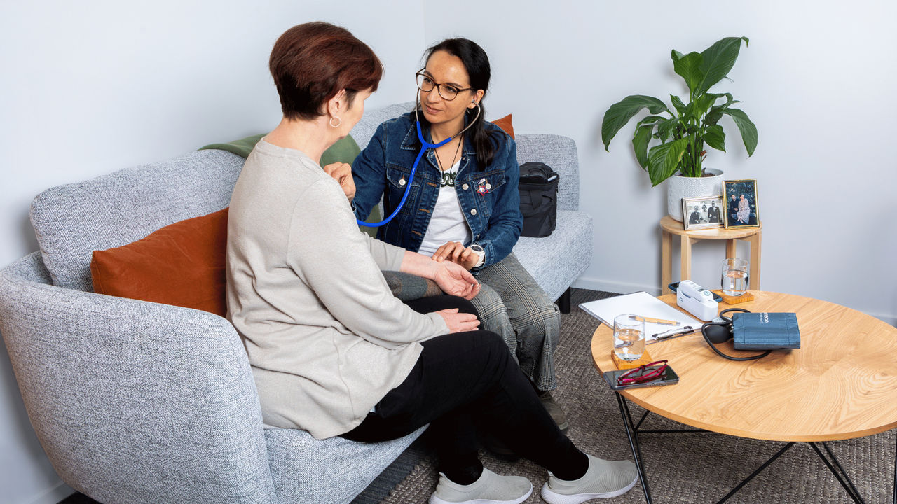 Nurse Practitioner sits with a patient on a couch while checking her pulse