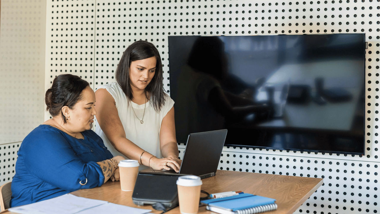 A manager uses a laptop to show a staff member how to complete an administrative task.