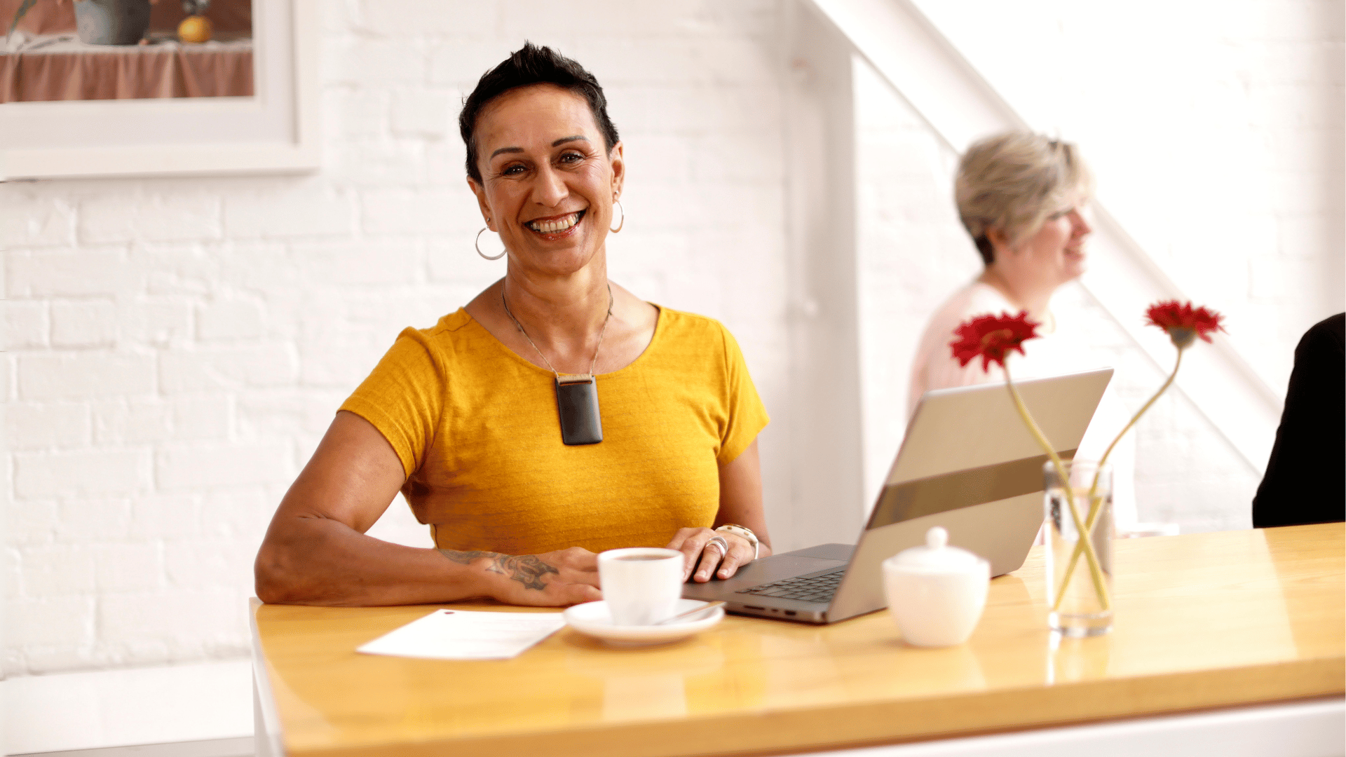 A smiling woman sitting at a table with a laptop, highlighting the varied career options available with a qualification in psychology.