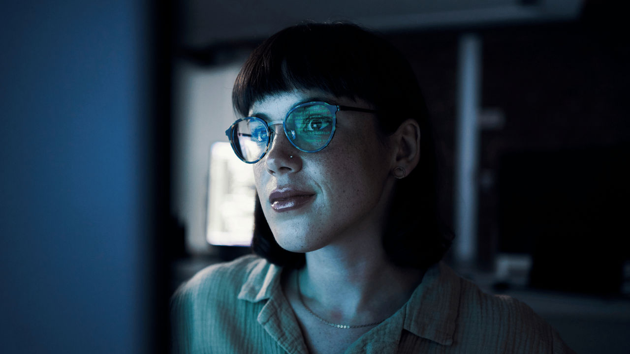 A UC Online Cyber Security student monitors online activity on a computer screen; lines of code are reflected in her glasses.