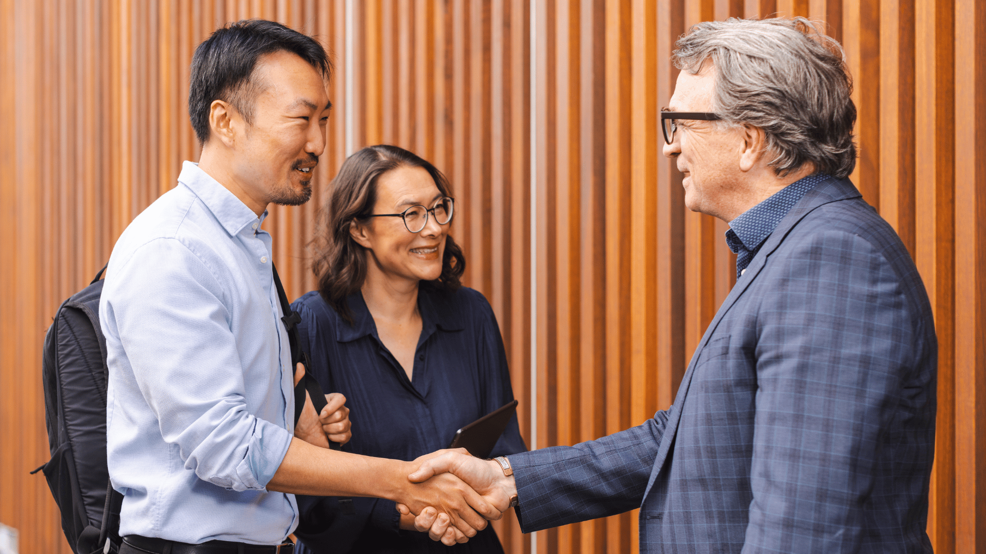 Two men shaking hands with a woman in the background as they discuss partnering with UC Online for their industry group training needs. 