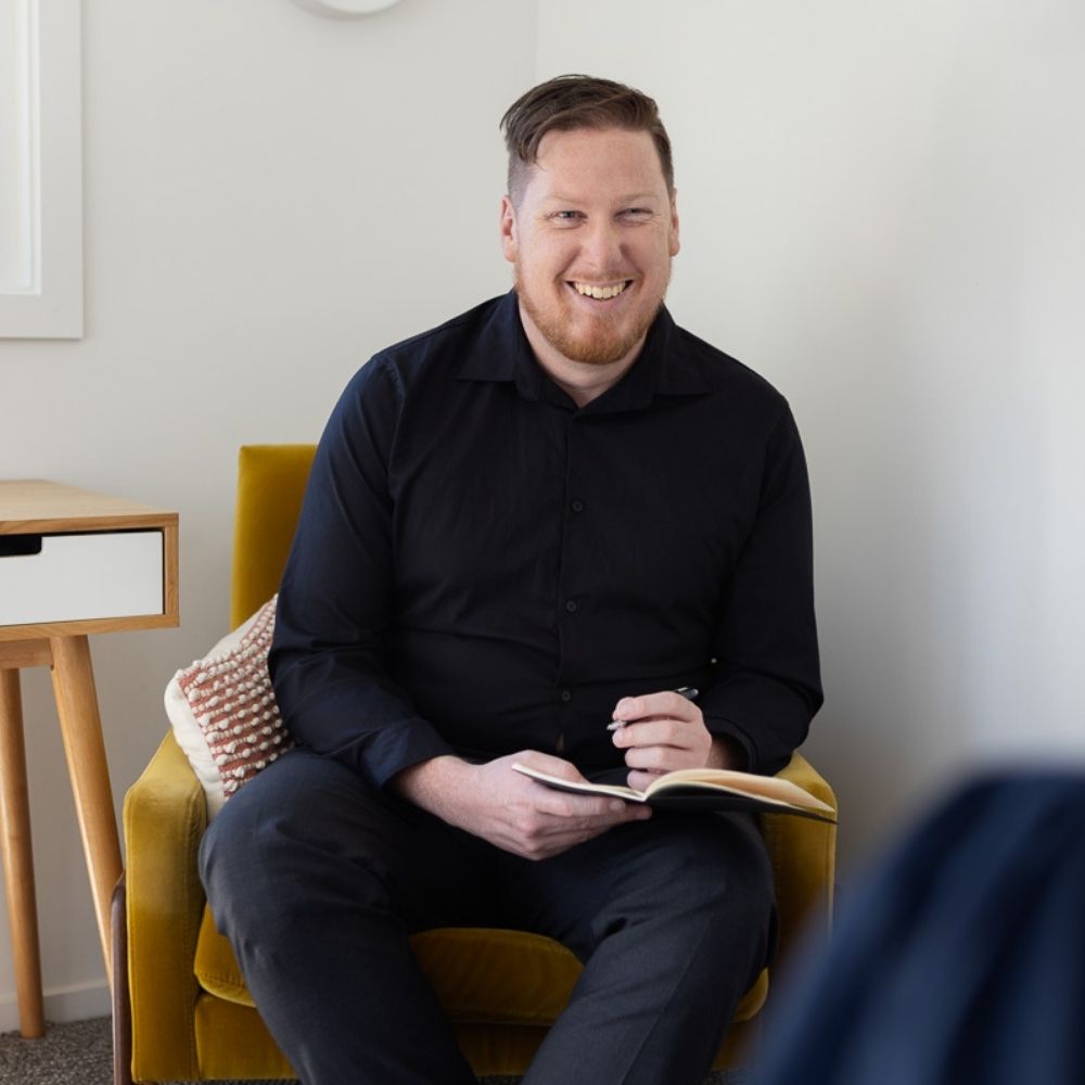 A man sitting in an armchair with a pen and notebook, illustrating the practical skills developed during the online graduate diploma in psychological science.