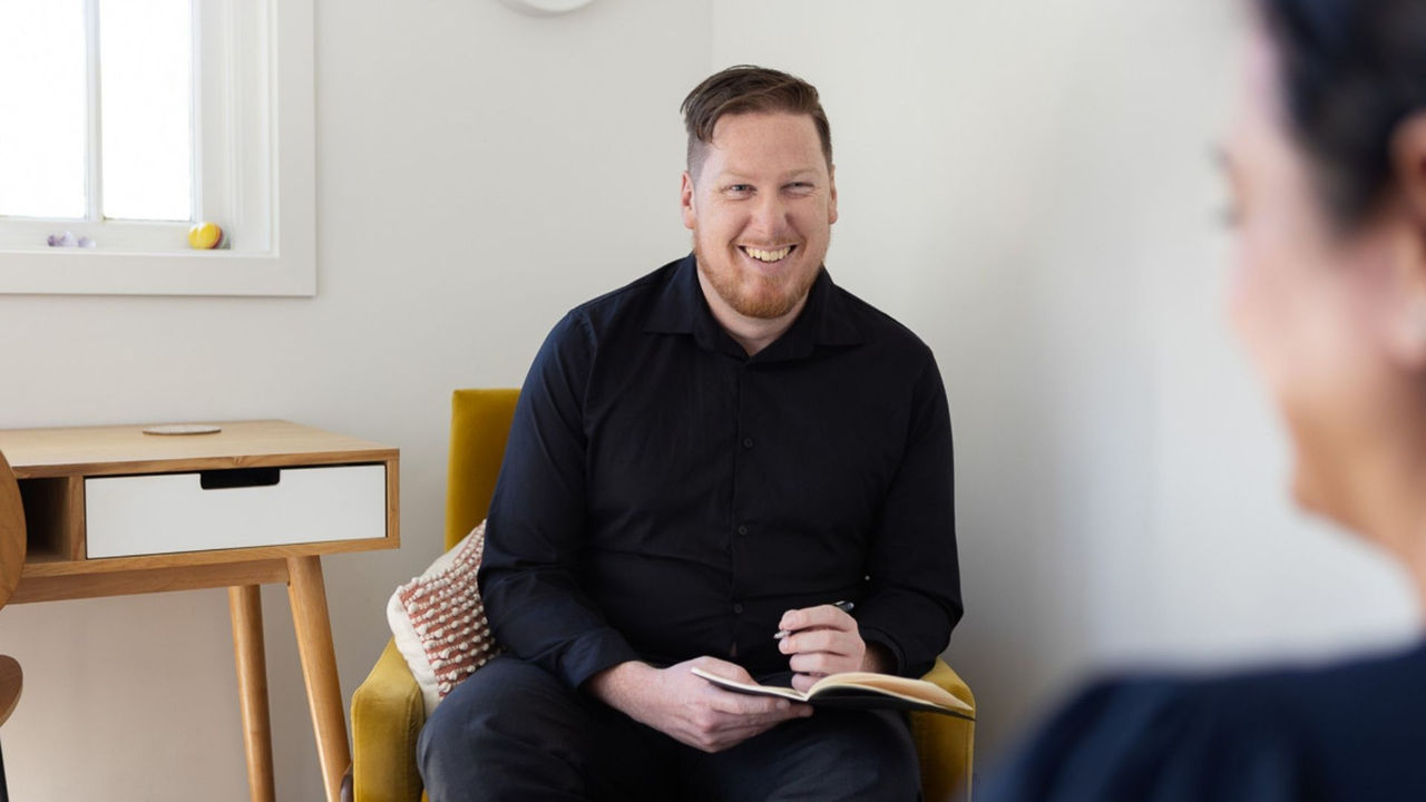 A man sitting in an armchair with a pen and notebook, illustrating the practical skills developed during the online graduate diploma in psychological science.