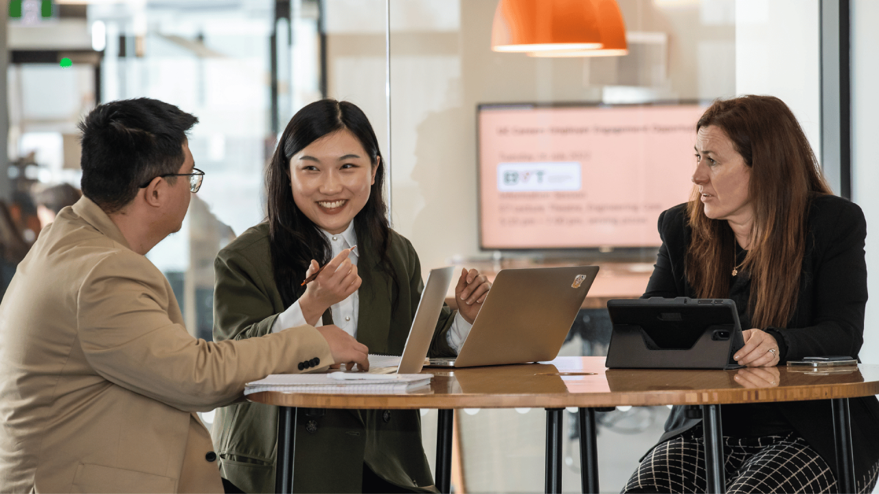 Three team members comparing cultural awareness course study notes in an open-plan office space. 