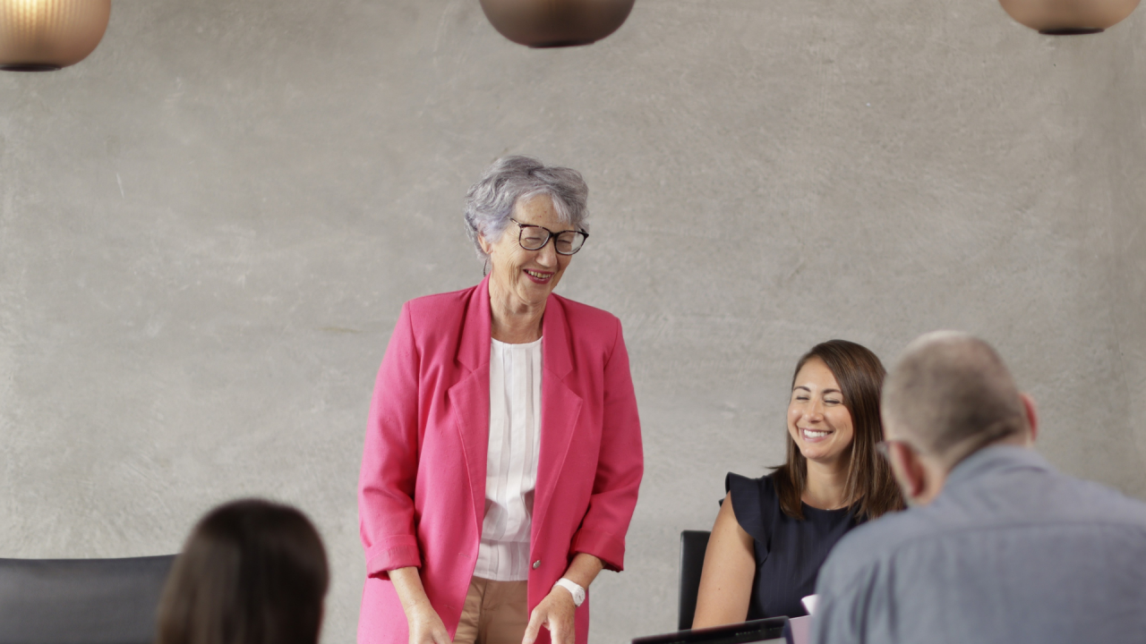 Improve your communication skills like this woman in an office environment talking to a colleague by studying Effective Communication for Work through Tuihono UC | UC Online