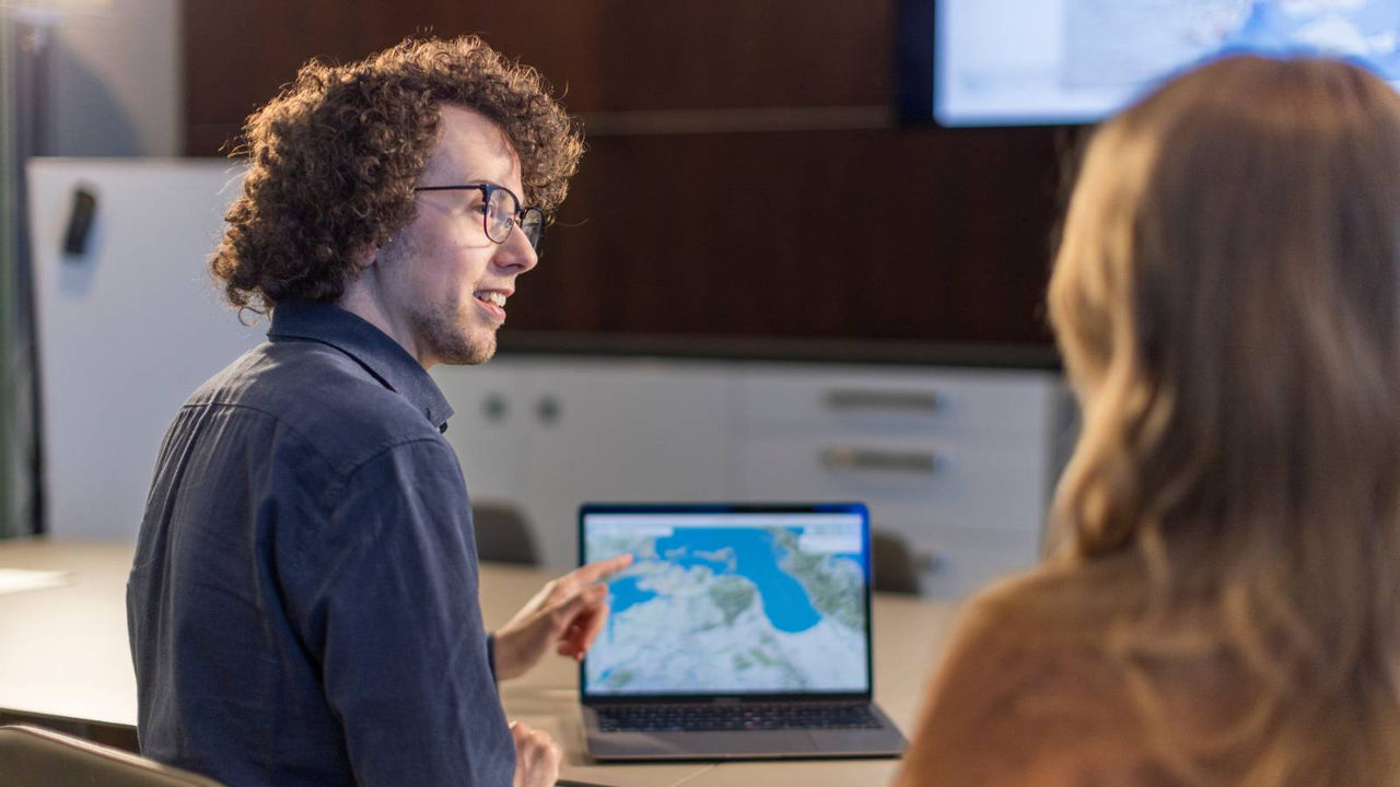 A GIS map on a computer screen is referred to by an analyst during a work meeting.