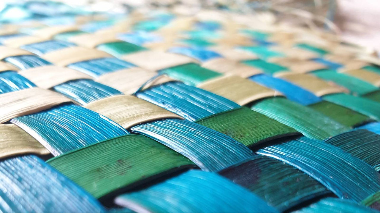 A harakeke (flax) weaving in bright colours of blue, green, and sandy brown. 